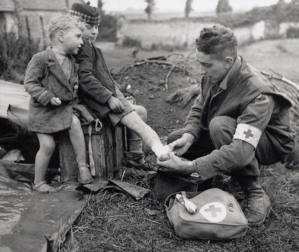 A medic bandages the injured foot of a child while his younger brother looks on.