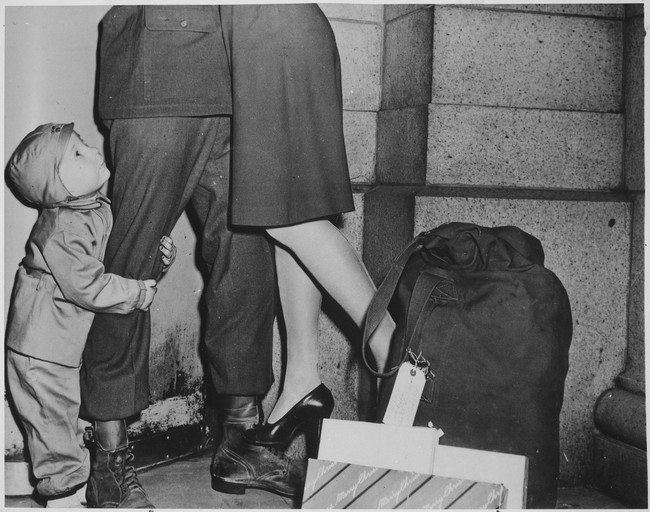 A youngster clutches his soldier father who's home for Christmas as he lifts his wife from the ground. 1944