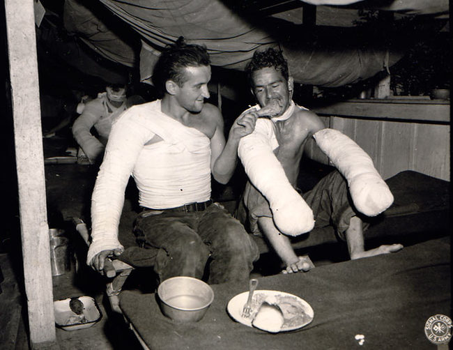 Sgt Edward Good helps his buddy eat Christmas dinner while in a Belgium field hospital. 1944
