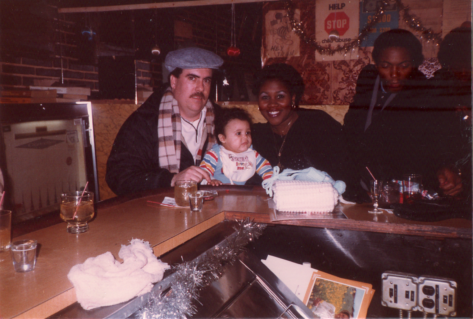 An infant with their mother & father at a bar because that's how parents rolled in the early '80s.