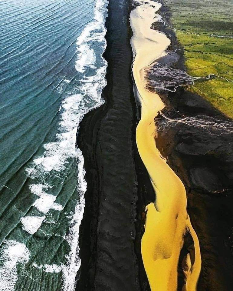 place in iceland where green fields yellow river black beach and blue sea meet