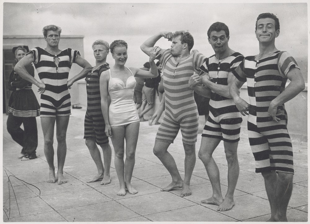 A group of people models beach wear from Victorian and Edwardian eras. One model shows off a contemporary (1940s) swimsuit.