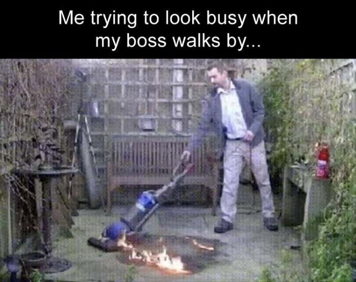 Funny meme about looking busy when boss walks by of a guy vacuuming a fire.