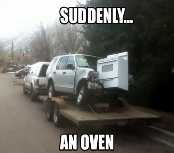 Car being towed on a trailer that crashed into an oven that is now stuck to the car.