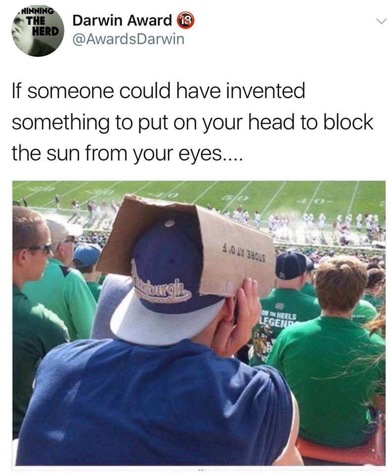 Man wearing his baseball hat backwards, but is using cardboard to block the sun up front.