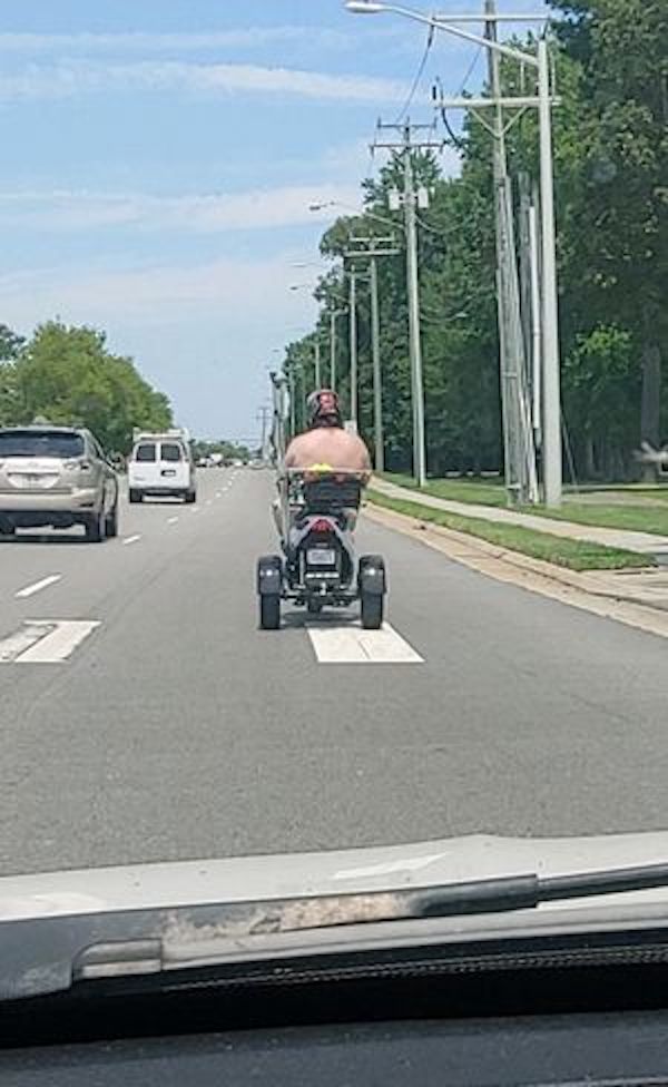 Shirtless guy driving a homemade gokart down the street