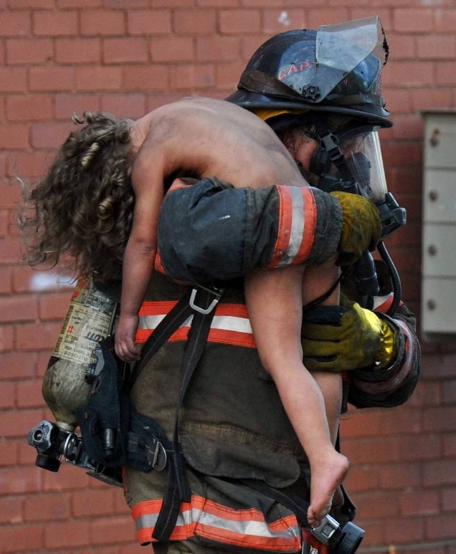 A fireman rescues an unconscious child from fiery hell.