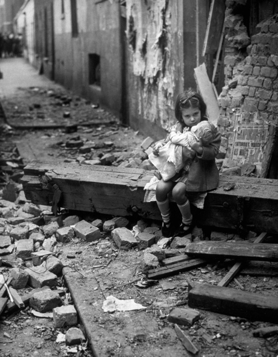 Little girl comforting her doll in the ruins of her bomb damaged home, London, 1940.