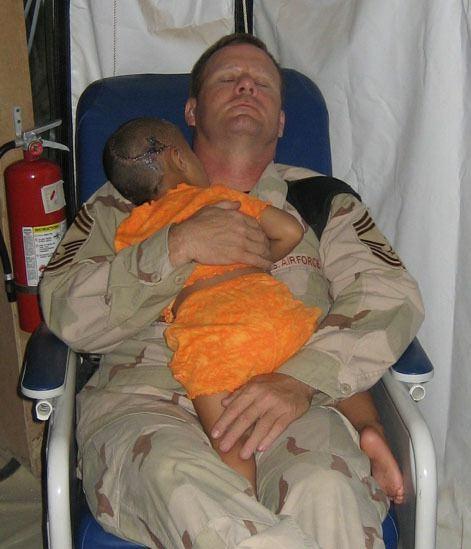 This US Soldier comforts an injured Iraqi child. Her entire family was executed and they intended to execute her as well with a shot to the head. They failed to successfully execute her.  US Soldier John Gebhardt was the only one the girl calmed down with, so he spent 4 nights holding her while they slept in that chair.