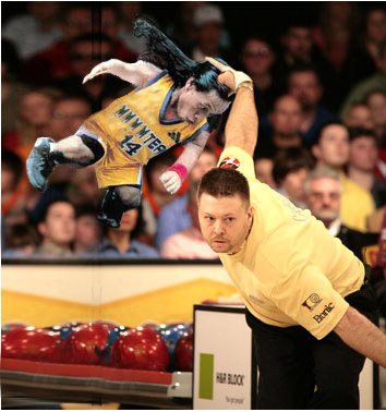 Midget being tossed down bowling alley lane in order to knock over pins at the end.