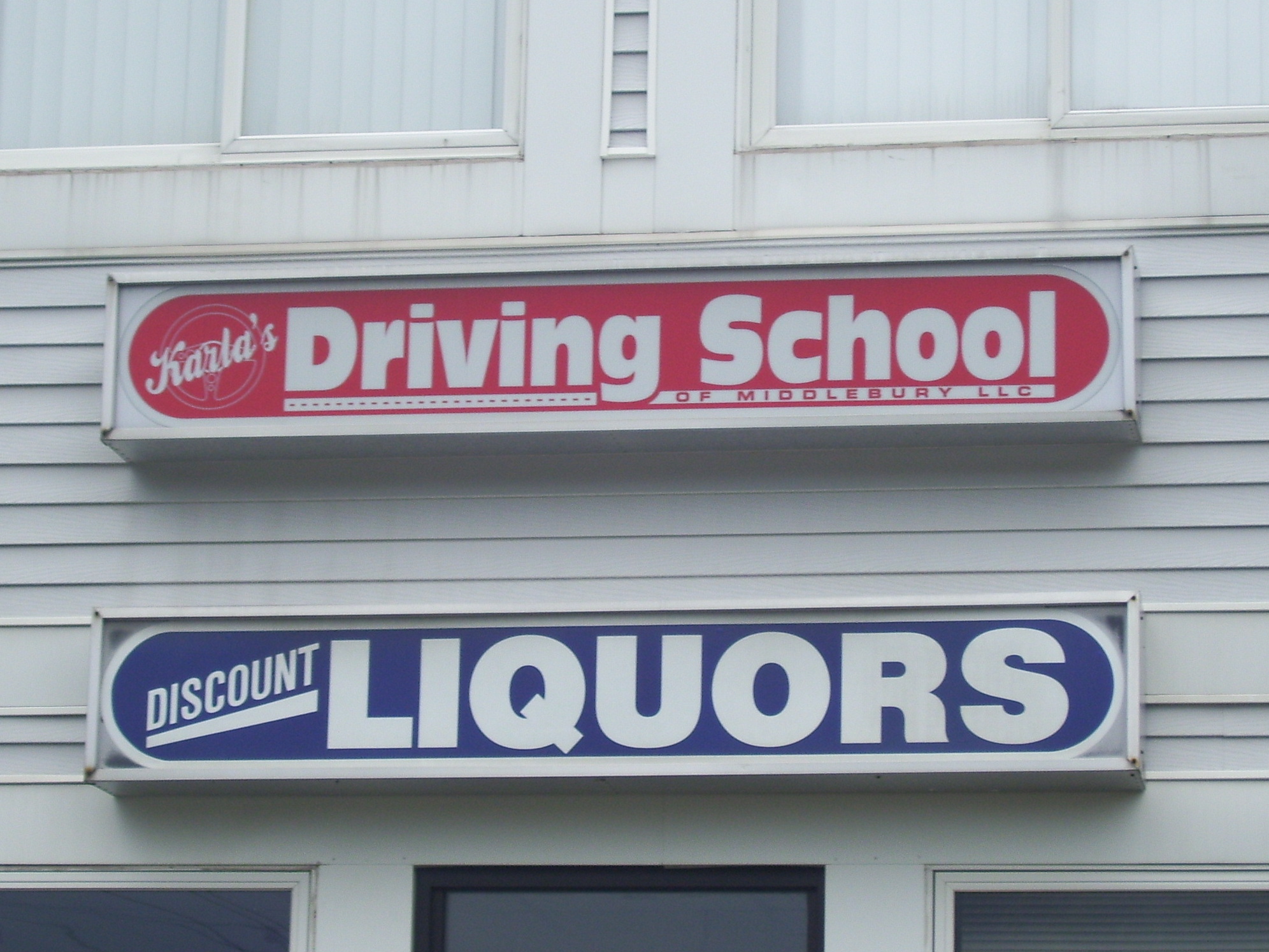 stores right next to each other, with signs above each other. Driving school and Discount liquors