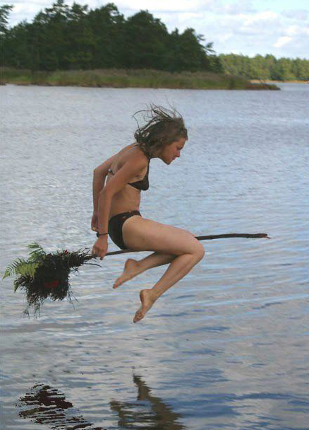 A witch flys across a lake on a broomstick