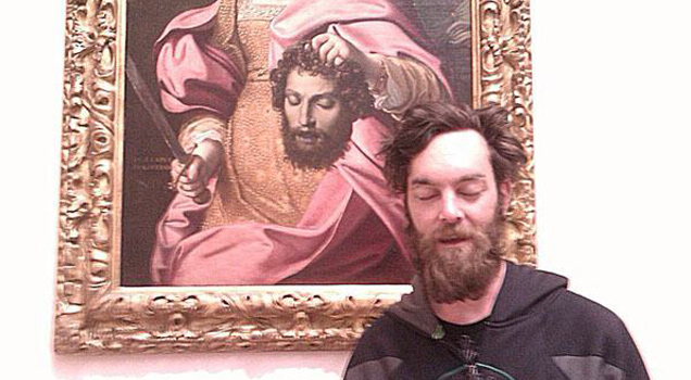 man standing in front of a painting of a royal person holding the head of a man who looks like the man standing in front of the painting.