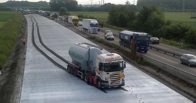 Truck sits in wet cement with trailing tire marks through the cement extending a football field's length.