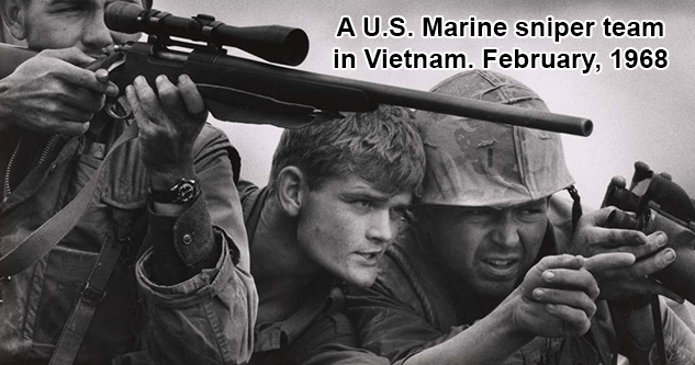 A U.S. Marine sniper team in Vietnam. February, 1968. A man looks down the scope of his rifle while two others look on, point, and discuss.