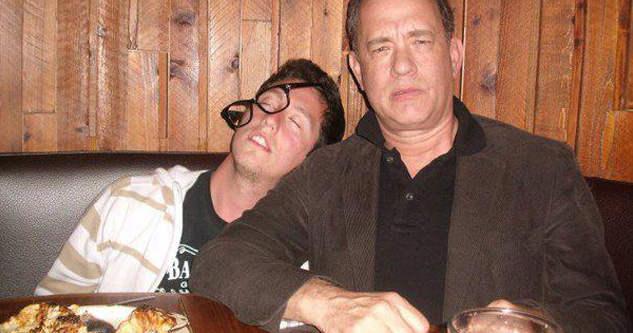 Tom Hanks sits with a drunk, passed out dude resting his head on his shoulder.