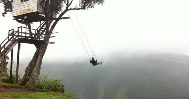 Guy swinging on a swing next to a tree house and above a cliff.