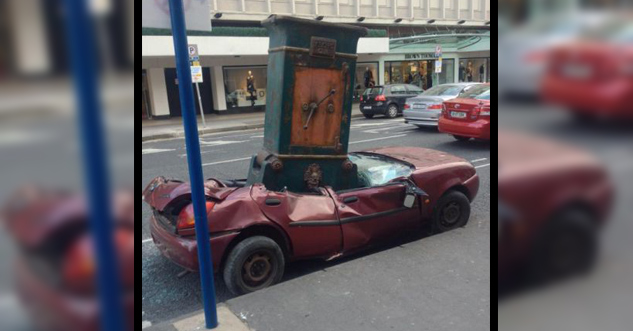 A parked car that has been crushed by a safe that is on top of it.