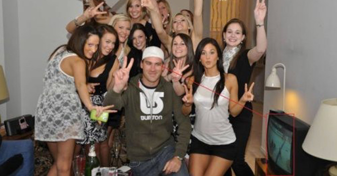 Guy poses for a picture with a bunch of babes, but he's watching hockey on TV.