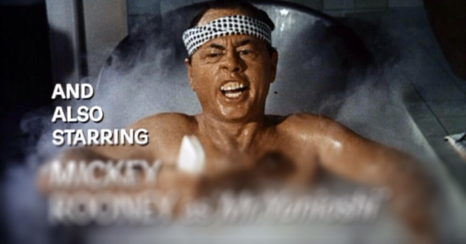 Mickey Rooney sitting in a bathtub, looking asian, wearing a hachimaki, curling his upper lip inward to expose his upper teeth, and holding a bar of soap. Text: and also starring Mickey Rooney as Mr. Yunioshi.