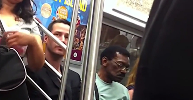 Keanu Reeves sitting on a crowded subway train.