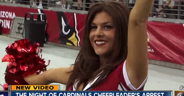 Cardinals Cheerleader shakes pompoms around on field. News titles cover bottom third of screen, but the text is illegible.