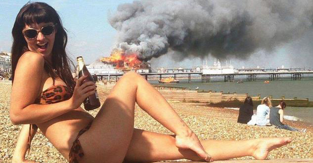 Hot woman in a bikini poses for camera in front of a burning boat in the background.