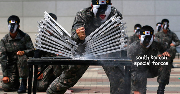 South Korean special forces breaking 10 layers of rock with his arm. He is wearing black and white war paint and a headband.
