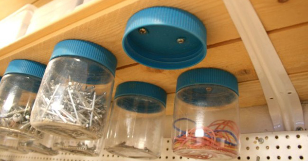 Jars screwed to the underside of a shelf. the jars are holding nails and things.