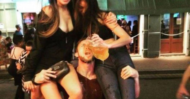 man picking up two women with one of them spilling beer on his face