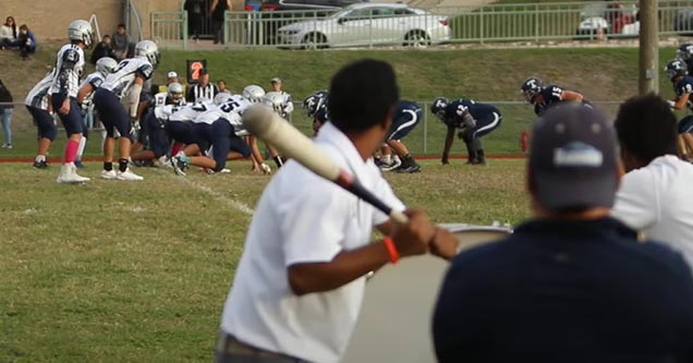 a coach holding a bat to hit a drum for the snap count for deaf football team