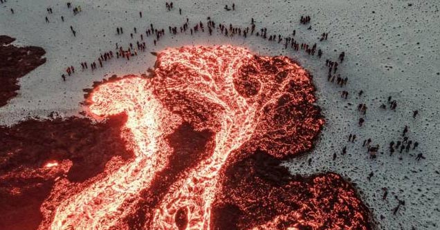 a crowd of people in norway gathered around a huge pool of lava