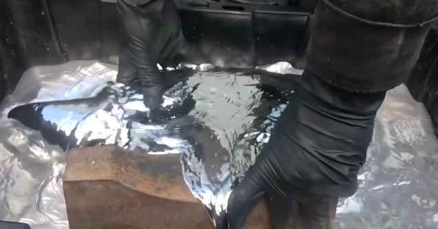 a man wearing black protective gloves puts an anvil into a tub of mercury