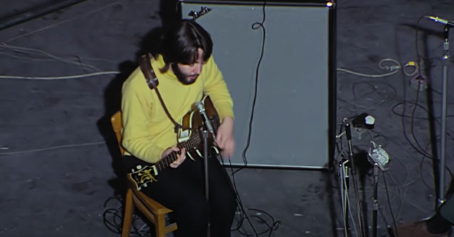 The Beatles: Get Back - Paul McCartney wearing a yellow sweater and playing the guitar