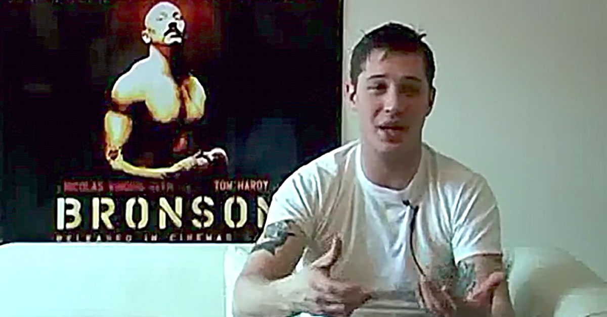 Tom Hardy sitting infront of a Bronson movie poster - talking about Charles Bronson