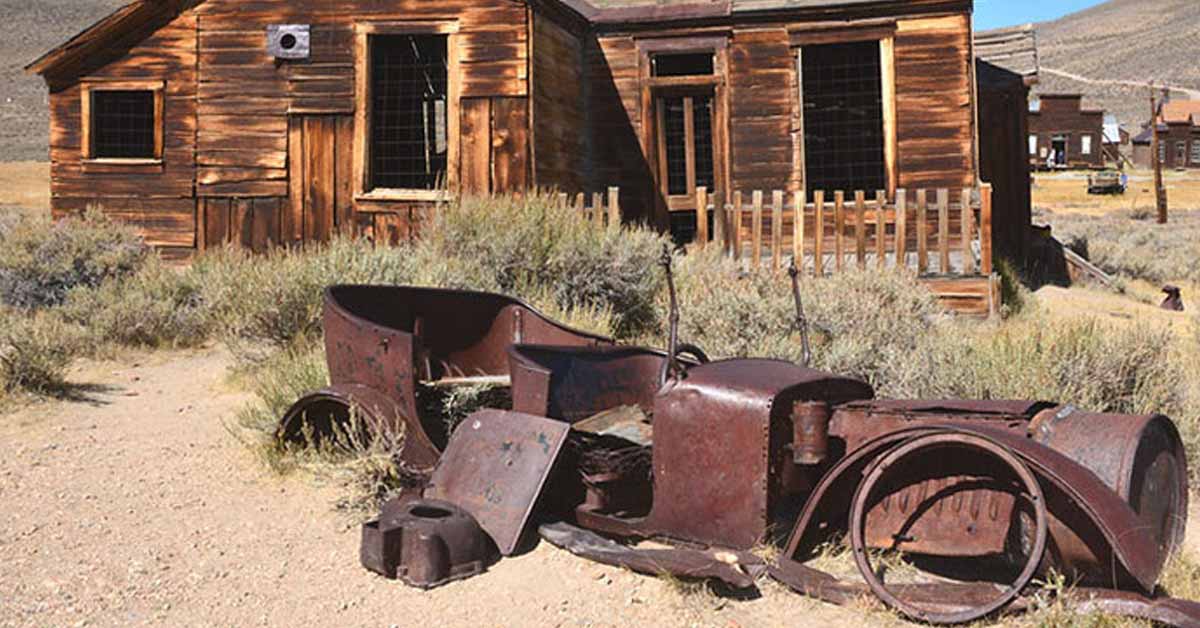 an old rusty car in front of a cabin