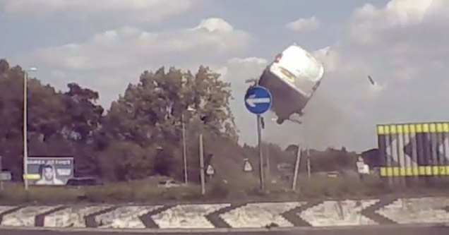 a white minivan way up in the air after hitting a roundabout